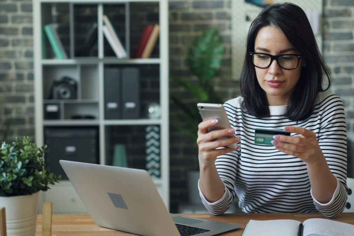 Woman sitting in front of the laptop with her debit card, wanting to buy something online, maybe she wants to improve her online shopping experience