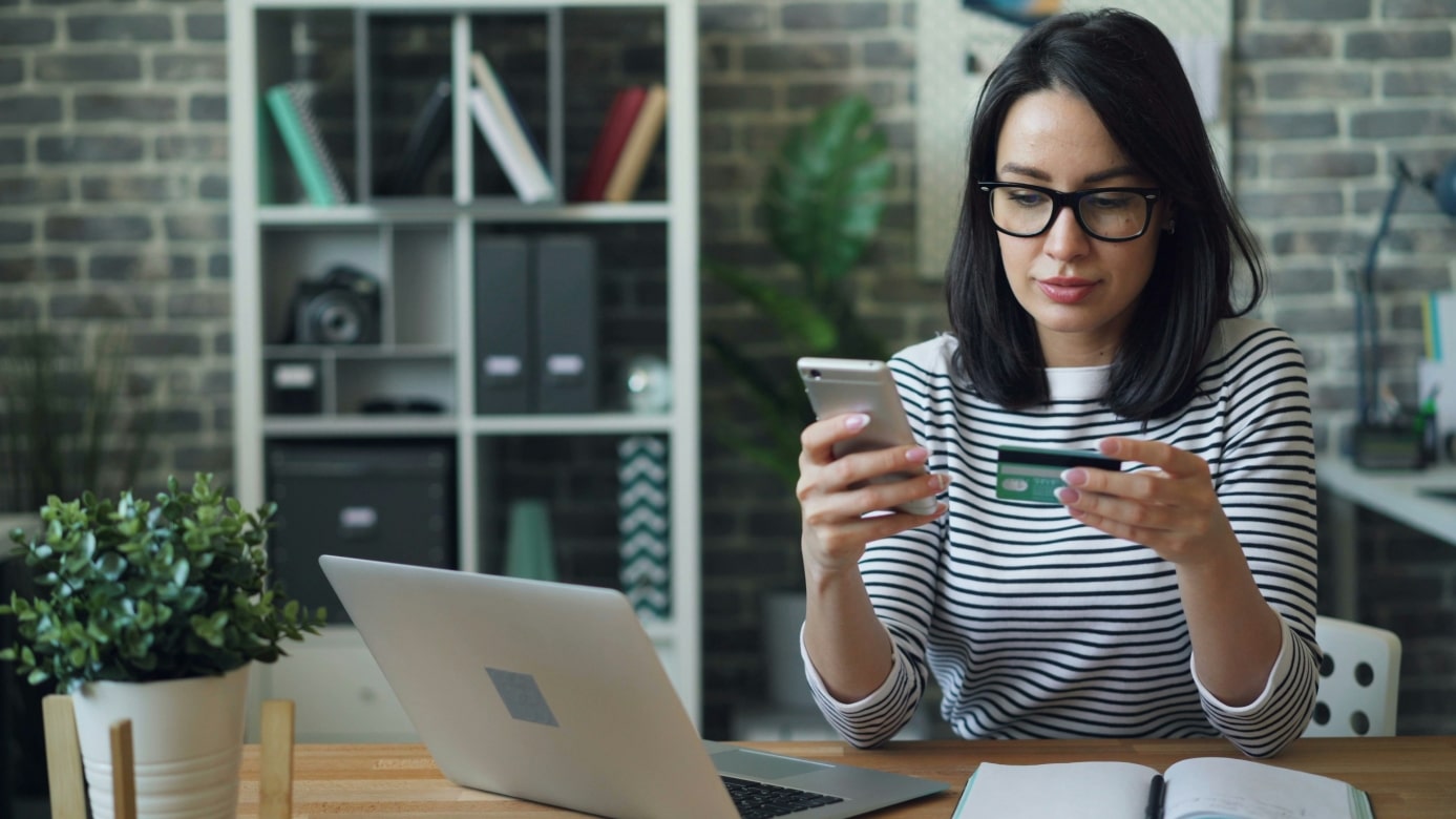 Woman sitting in front of the laptop with her debit card, wanting to buy something online, maybe she wants to improve her online shopping experience